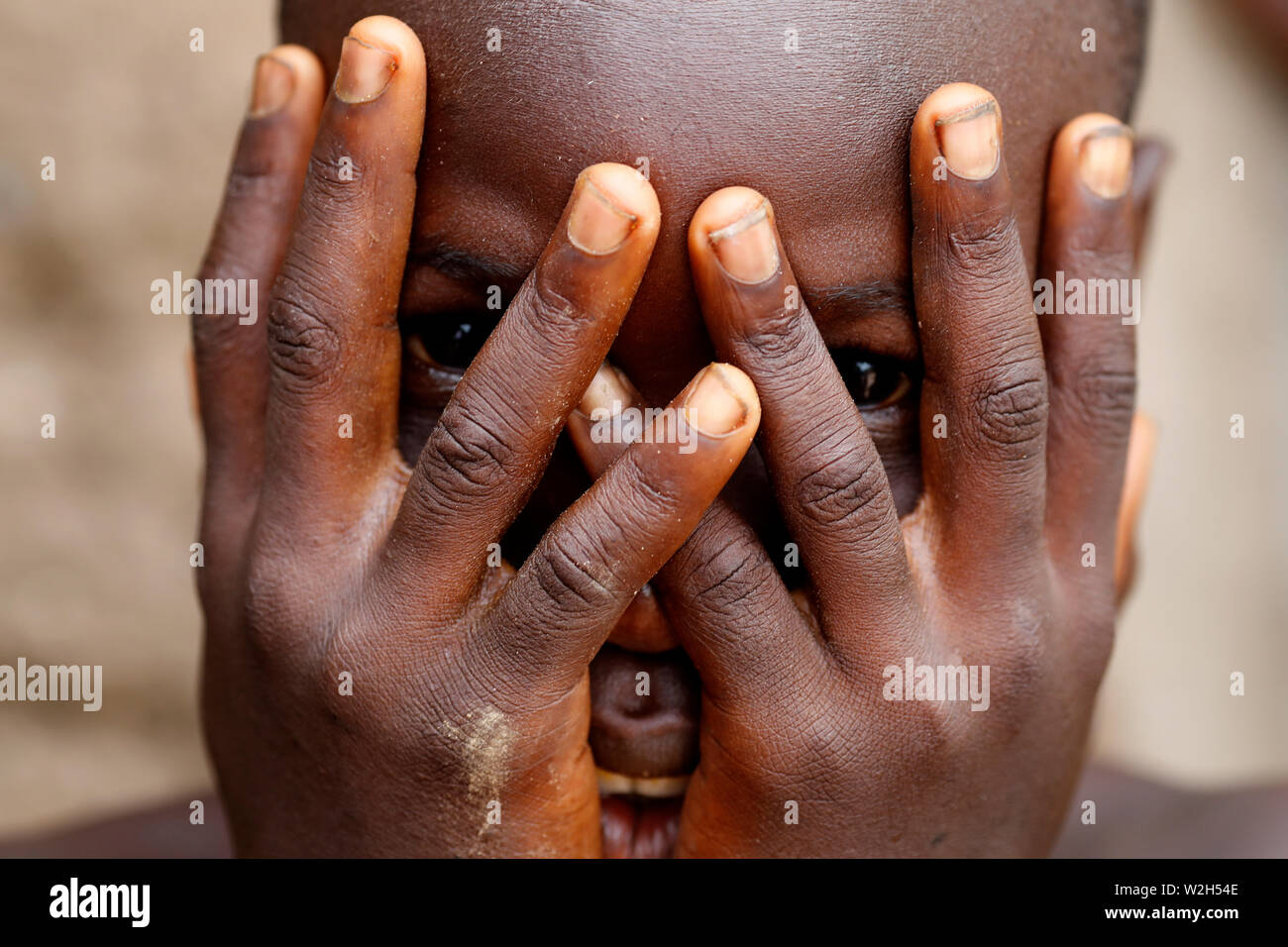 Africani scuola primaria. Ragazzo africano che ricopre la faccia con le mani, spiata attraverso dita alla fotocamera. Datcha-Attikpaye. Il Togo. Foto Stock