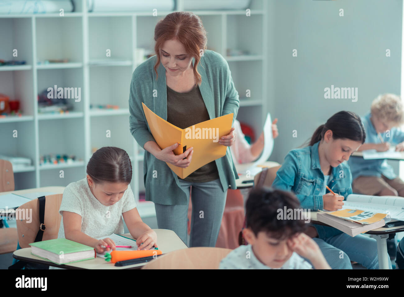 Insegnante attento cerca vicino al suo alunni opere. Foto Stock