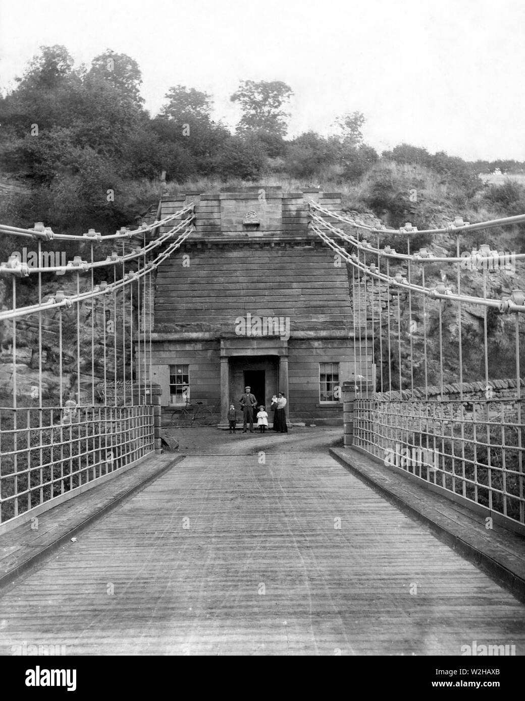 L'Unione Chain Bridge e casa di pedaggio sul lato italiano del ponte. La fotografia è stata scattata a circa 1899/1900 e con la famiglia Roxburgh al di fuori della loro casa. Casa del pedaggio è stata demolita negli anni cinquanta. Il ponte ancora trasporta traffico veicolare ed è il più antico ponte di sospensione in tutto il mondo continuano a farlo. Attraversando il fiume Tweed che collegano l'Inghilterra e la Scozia. Il ponte è nei pressi del villaggio di Berwick upon Tweed ed è stato progettato dal capitano Samuel Brown RN. Foto Stock