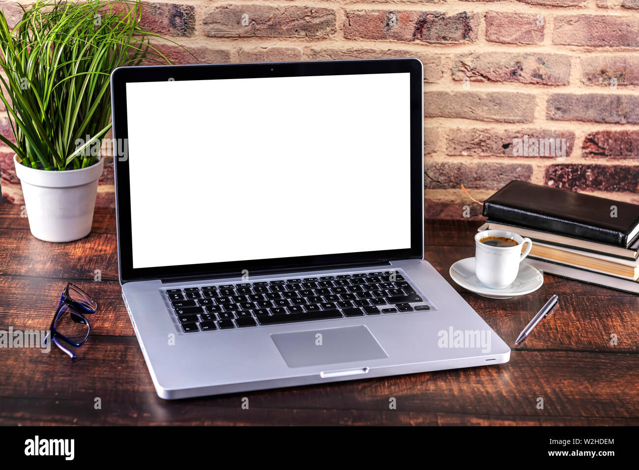 Laptop notebook con schermo vuoto e la tazza di caffè e blocco note e penna libri su un tavolo di legno. Mock up sul tavolo di legno con il computer portatile con schermo vuoto Foto Stock