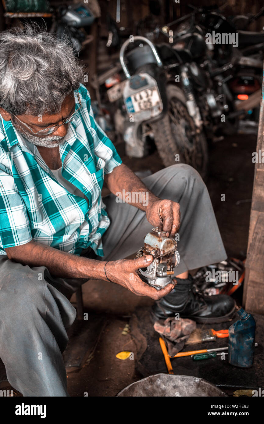 Un meccanico in una piccola officina in India, la riparazione del carburatore su una vecchia motocicletta. Foto Stock