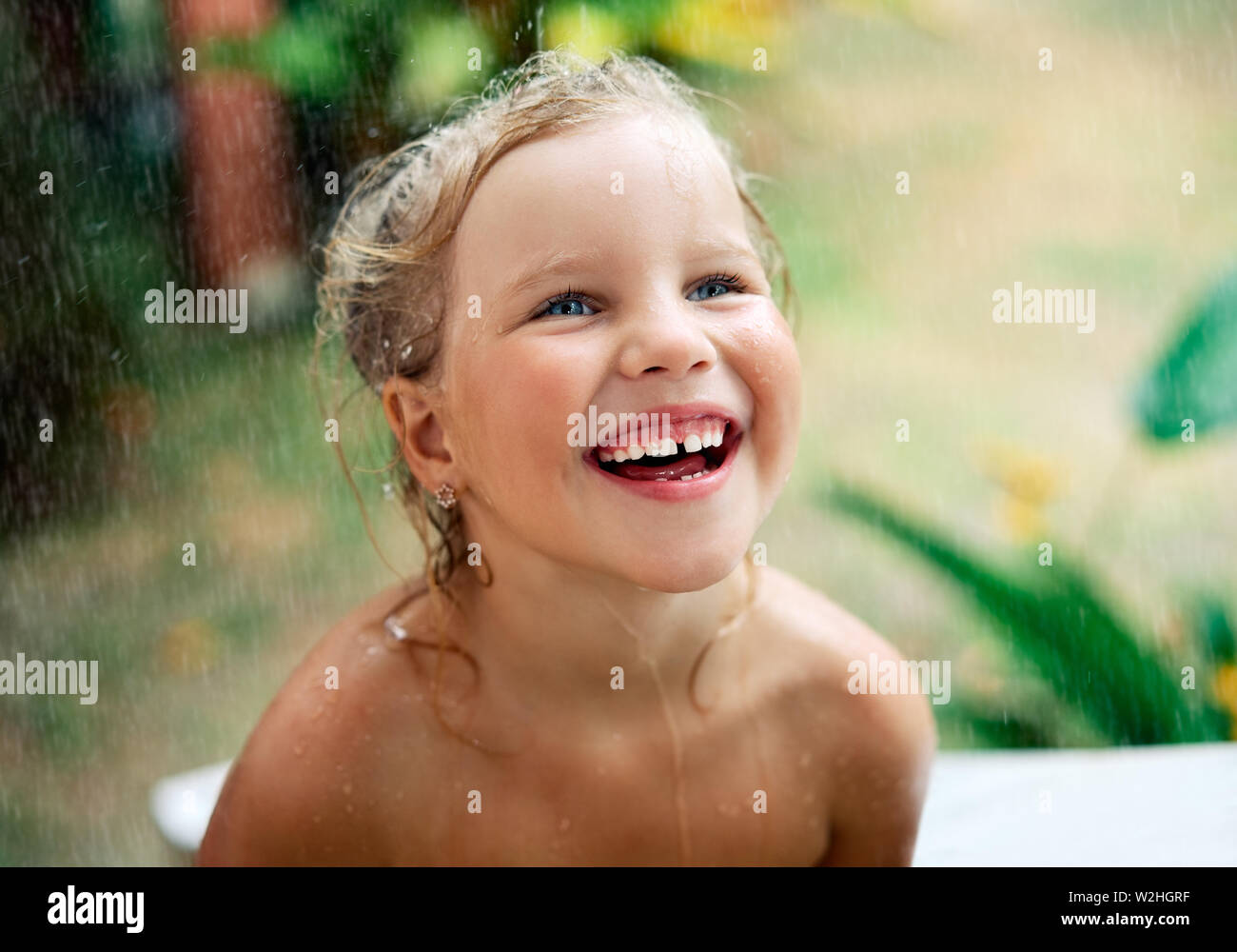 Close up ritratto di felice carino bambina godere della pioggia di estate. Gocce cadono sul suo viso, bambino sorridente. infanzia, emozioni e il concetto di vacanza Foto Stock
