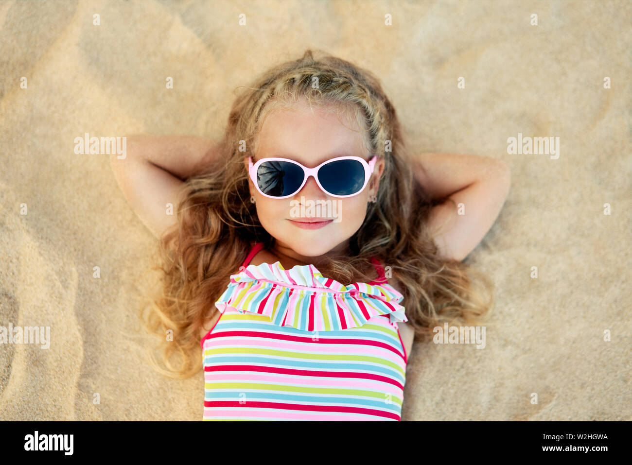 Vista superiore della bella ragazza bionda in occhiali da sole sdraiati  sulla spiaggia di sabbia durante le vacanze estive. Relax sul mare,  infanzia felice concetto Foto stock - Alamy