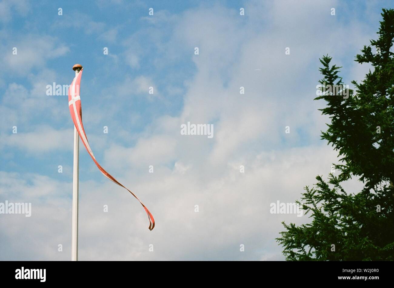 Bandiera danese battenti nel vento contro un cielo blu con un luminoso bianco delle nuvole. Foto Stock