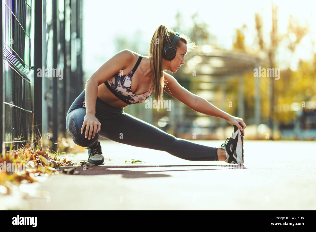 Giovani femmine runner con le cuffie sulle orecchie di lei, sta facendo esercizio di stretching nelle vicinanze di recinzione metallica. Ella è le riparazioni per allenamento mattutino. Foto Stock