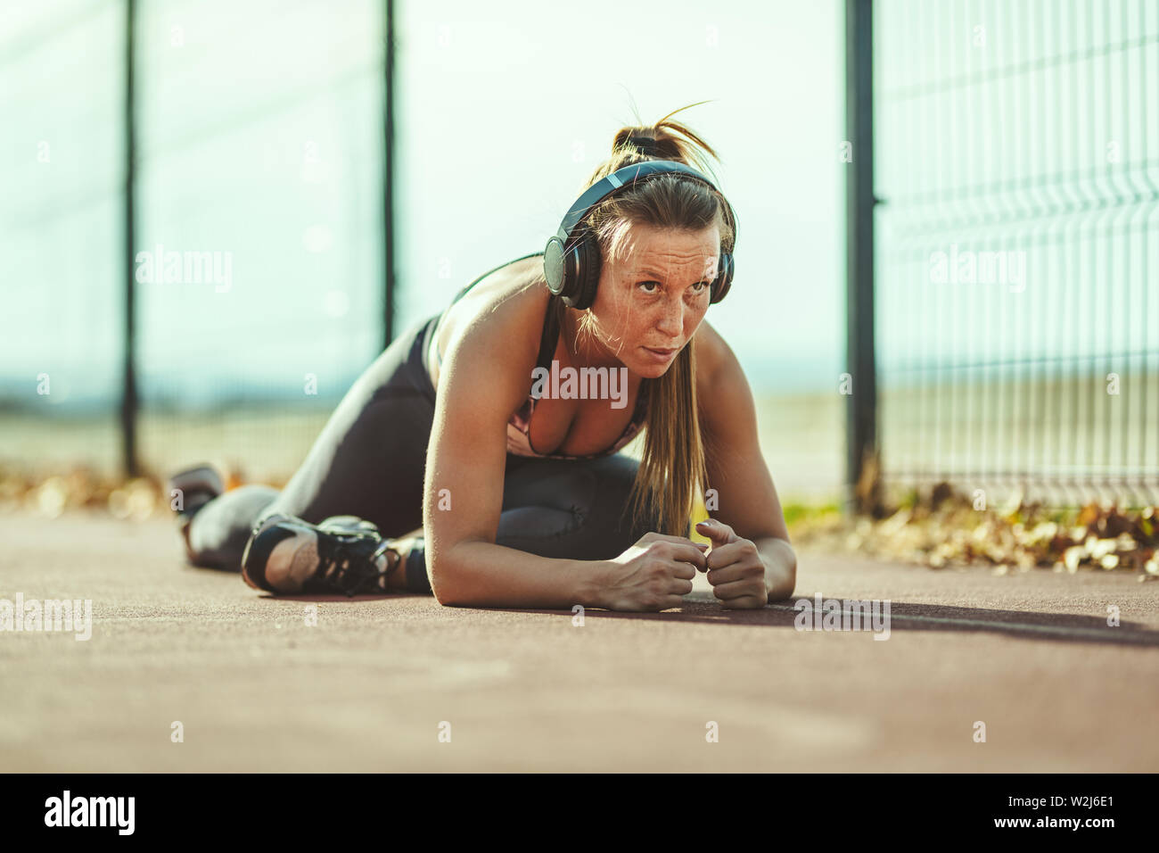 Giovani femmine runner con le cuffie sulle orecchie di lei, sta facendo esercizio di stretching nelle vicinanze di recinzione metallica. Ella è le riparazioni per allenamento mattutino. Foto Stock