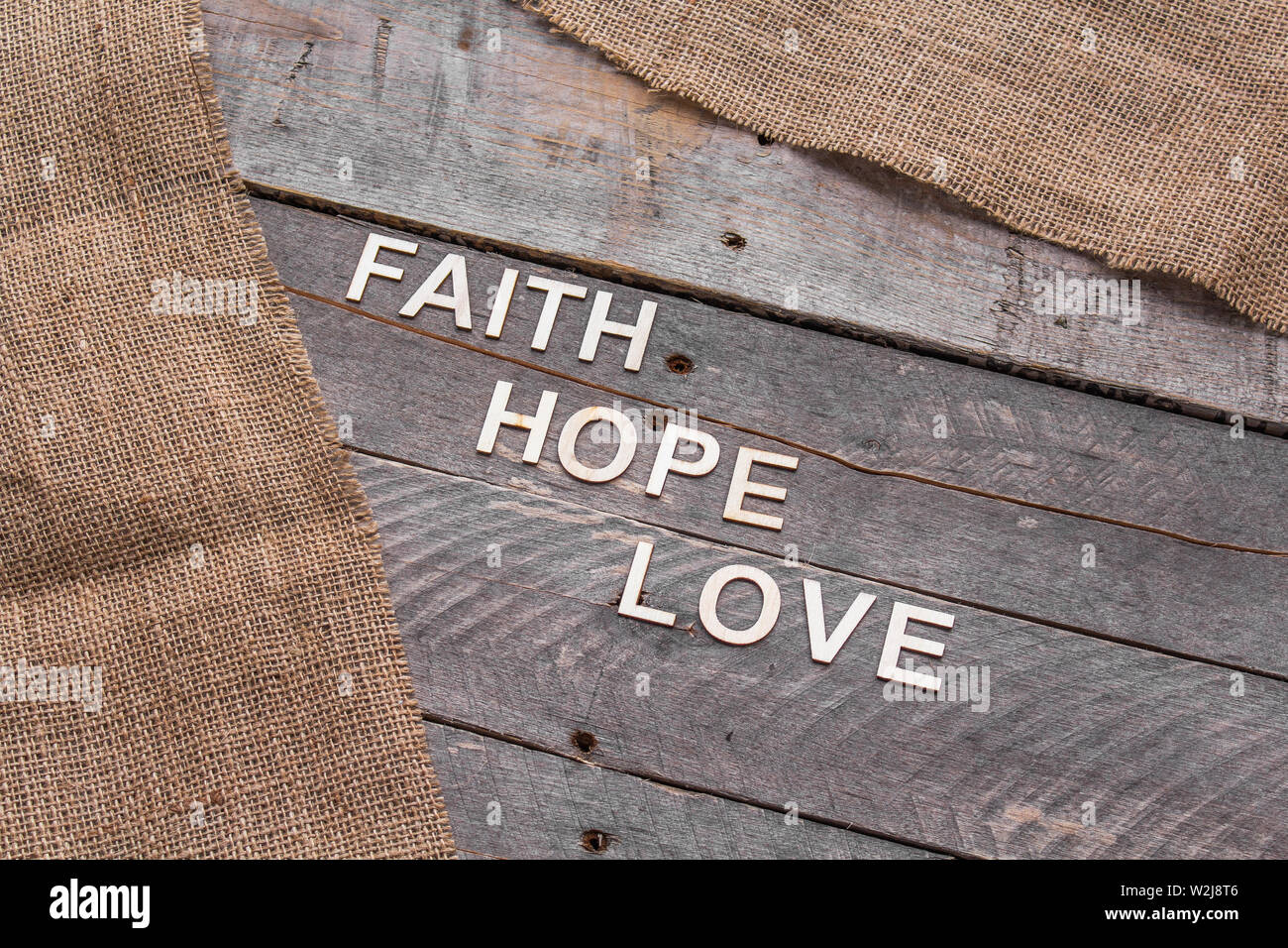 Sfondo rustico con mazzi e tela con le parole di fede, di speranza e di amore enunciato nelle lettere di legno Foto Stock