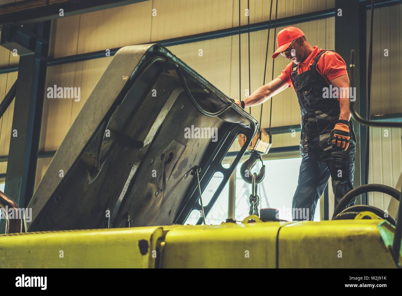 Caucasian meccanico nel suo 30s riparazione escavatore. Guardando sotto il coperchio motore. Tema industriale Foto Stock