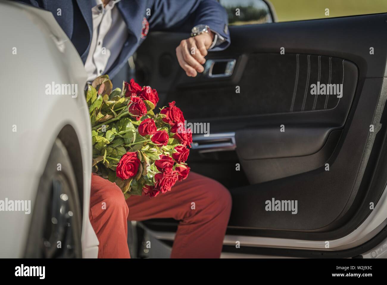 Uomini caucasici con mazzo di rose rosse in attesa del suo amante mentre posti a sedere in un moderno e sportivo auto. Costruire il concetto di relazione. Foto Stock