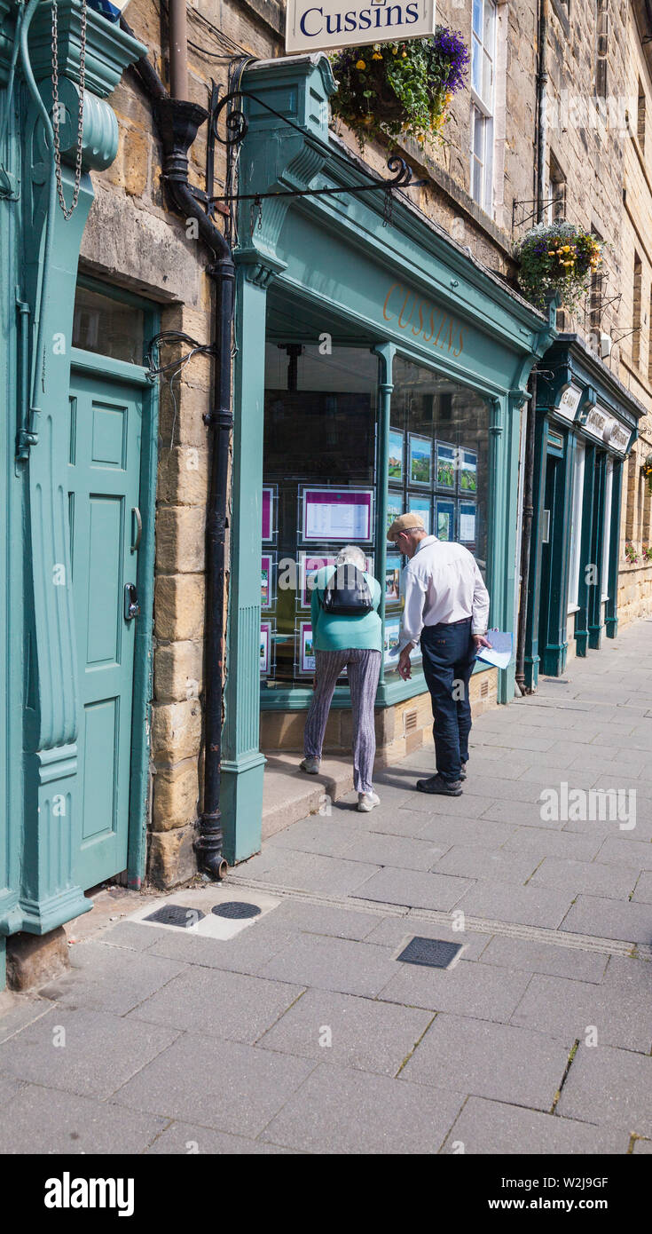 Una coppia matura cercando nella finestra di Cussins, un locale di agenti immobiliari in Alnwick,Northumberland,l'Inghilterra,UK Foto Stock