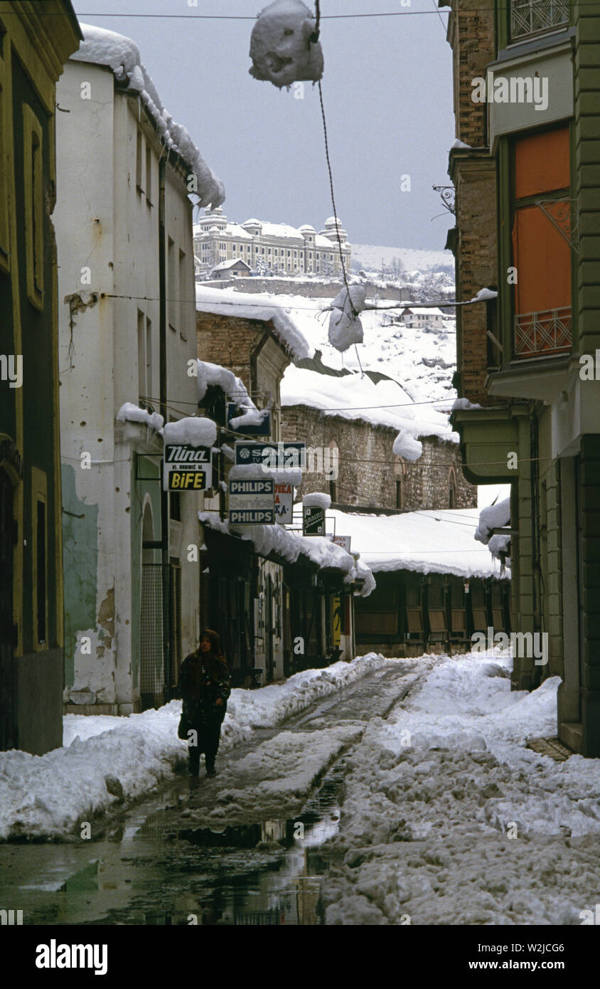 Il 28 marzo 1993 durante l'assedio di Sarajevo: una vecchia donna cammina lungo Kundurdziluk Street nella città vecchia. Sulla sommità della collina in background è Jajce caserma militare. Foto Stock