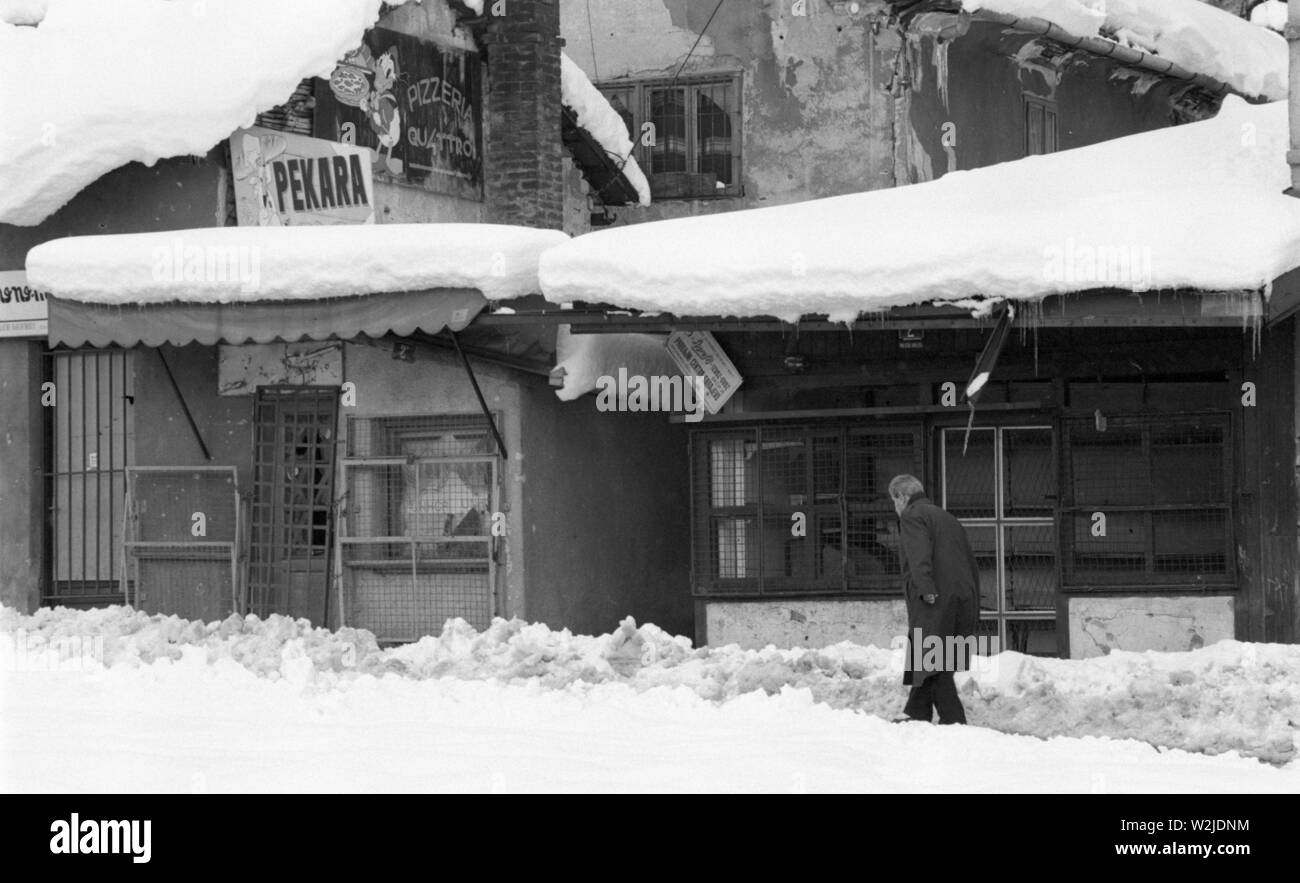 Il 28 marzo 1993 durante l'assedio di Sarajevo: un vecchio uomo cammina su un percorso attraverso la neve profonda passato squallidi negozietti, tutte chiuse fino in piazza in Bascarsija. Foto Stock