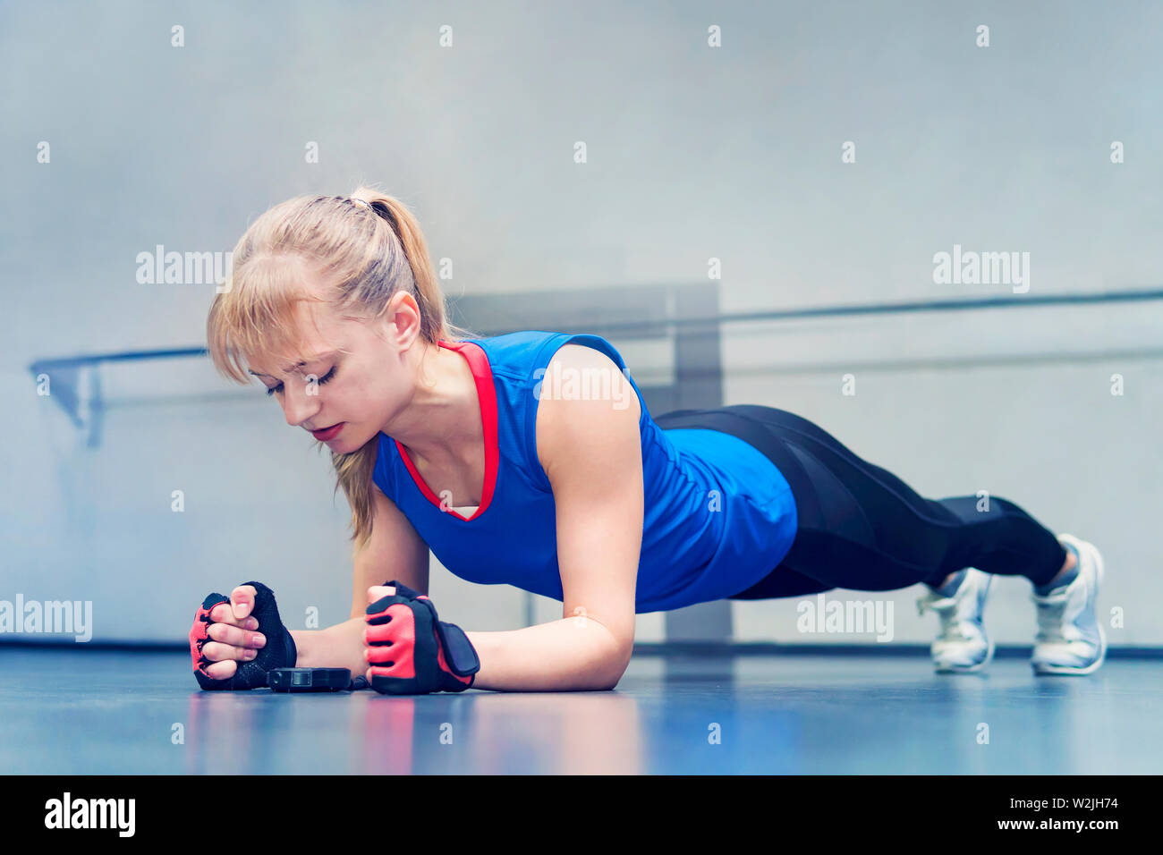 Donna facendo push-up esercizio. Femmina forte facendo crossfit allenamento. bionda si erge sul suo gomiti e guarda il cronometro sul pavimento. endurance Foto Stock