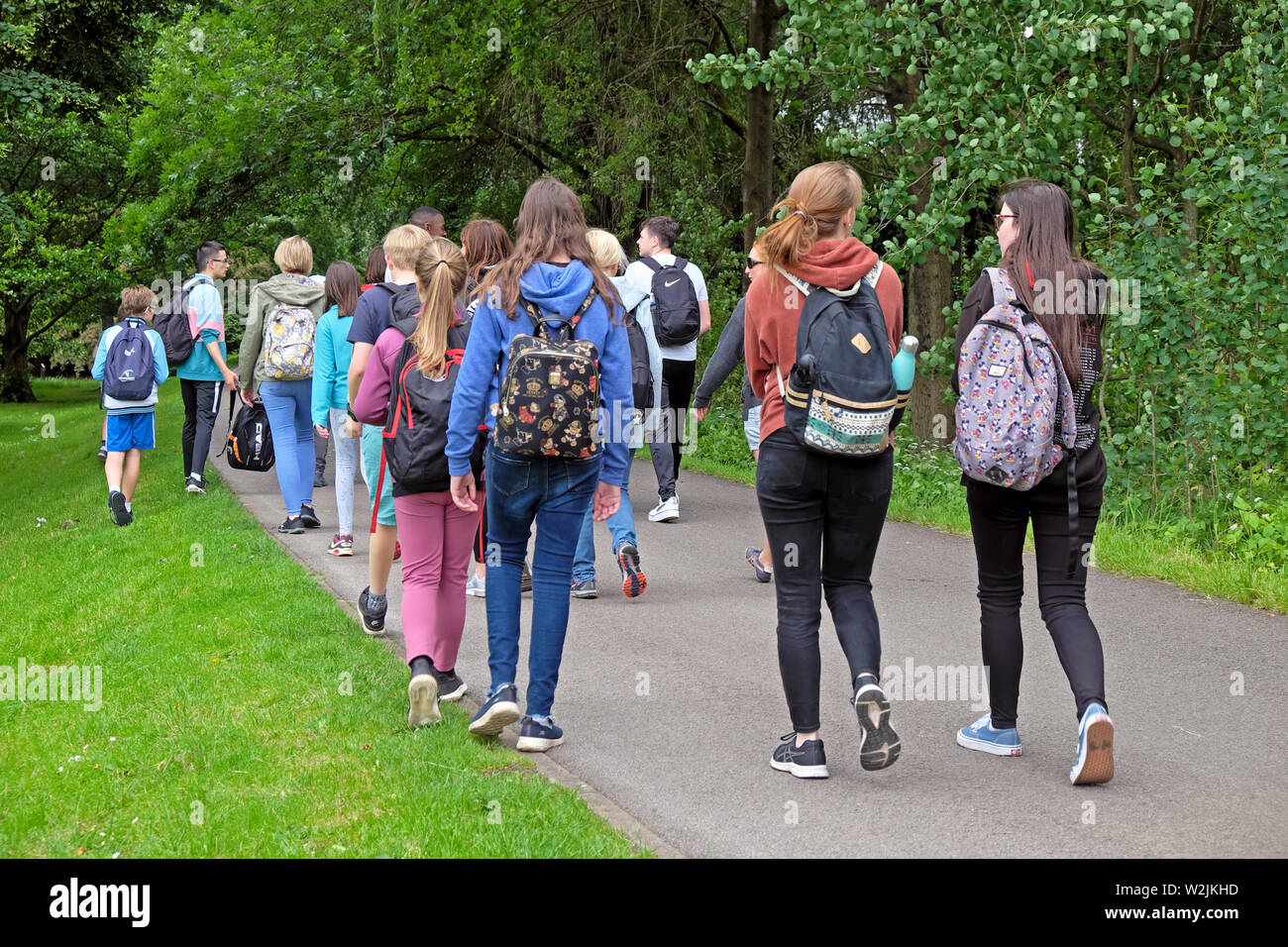 Gruppo di giovani studenti ragazzi con zaino vista posteriore camminare all'aperto in estate a Bute Park Cardiff Wales UK KATHY DEWITT Foto Stock