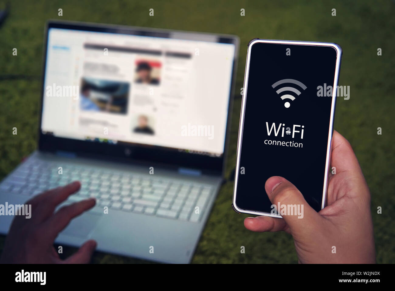 Smartphone con connessione wifi icona generica sullo schermo attesa da uomo sullo sfondo del display del computer portatile e la tastiera. L'uomo utilizza hot spot Wi-Fi per Foto Stock