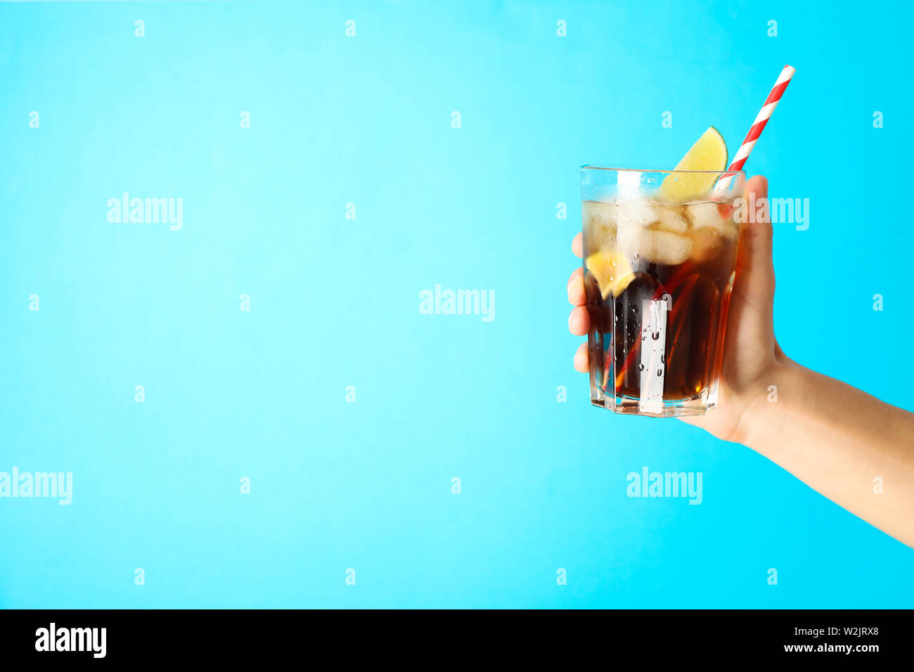 Femmina di mano in mano un bicchiere con ghiaccio cola, tubulo calce e slice Foto Stock