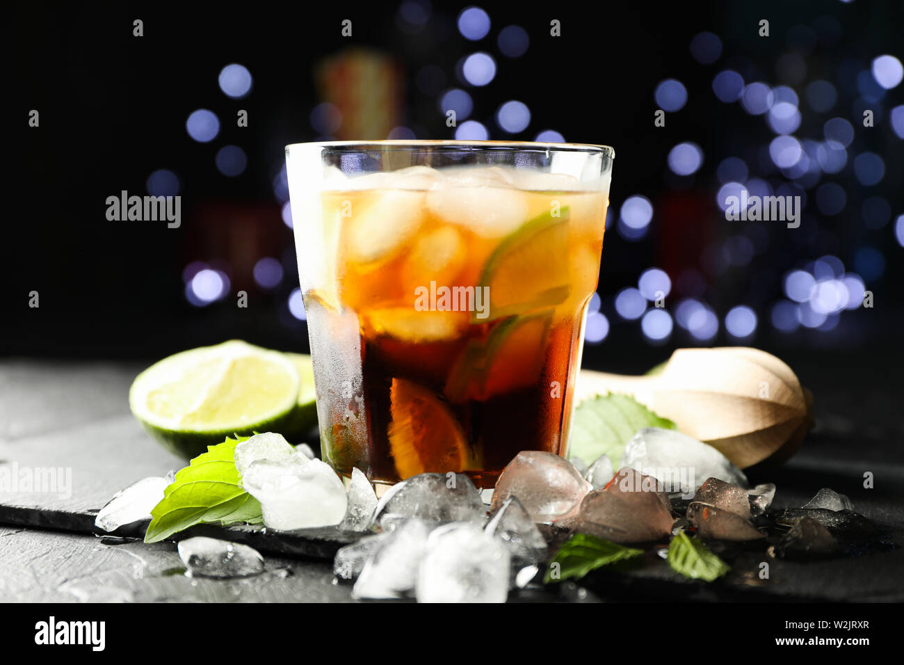 Vetro con cola e fettine di lime, spremiagrumi, ghiaccio, menta contro sfocata sullo sfondo delle luci Foto Stock