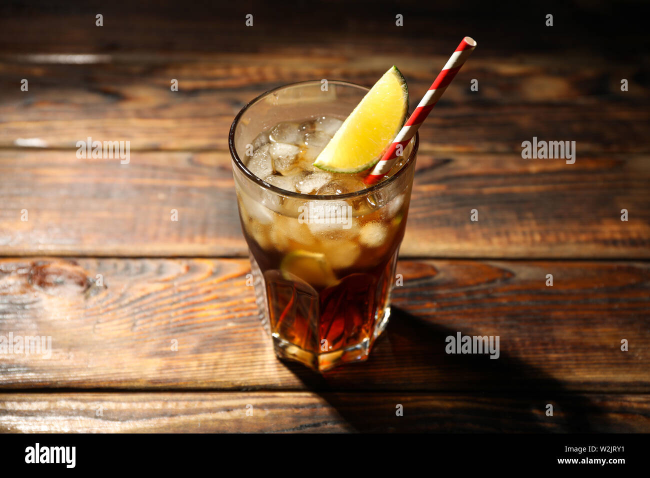 Bicchiere con ghiaccio cola e calce fetta su sfondo di legno Foto Stock