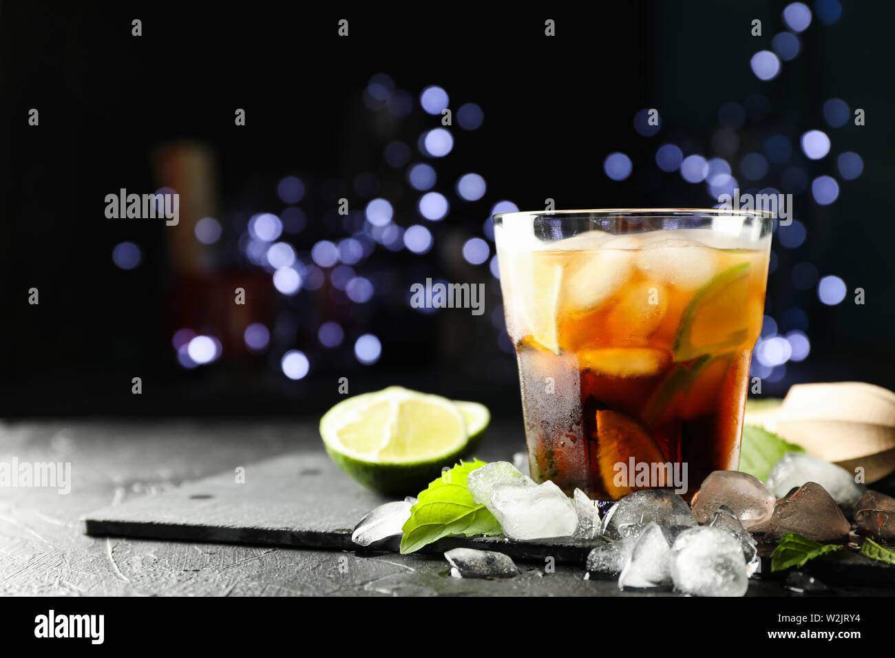 Vetro con cola e fettine di lime, spremiagrumi, ghiaccio, menta contro sfocata sullo sfondo delle luci Foto Stock