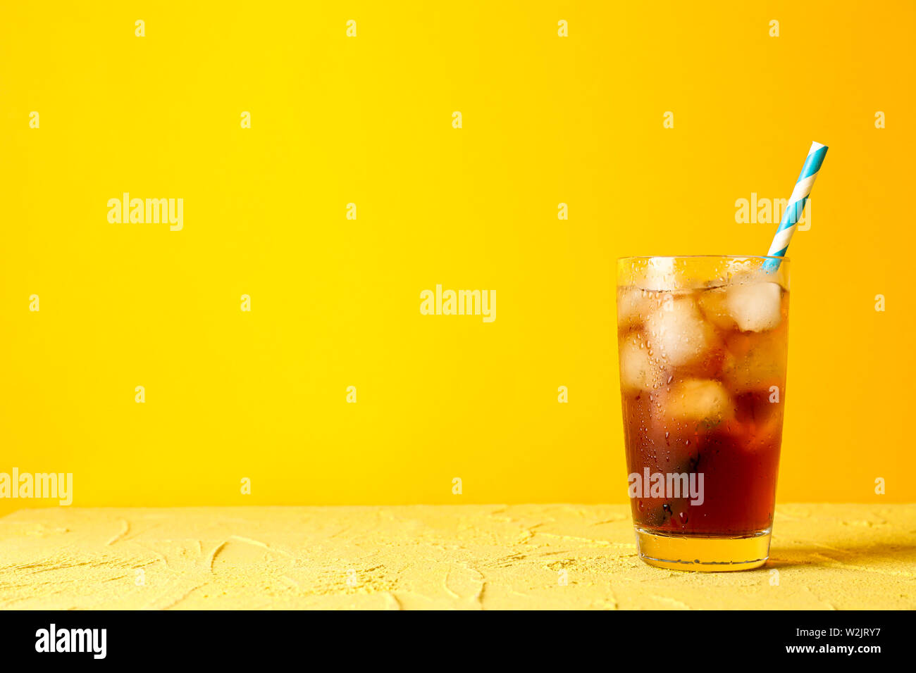 Vetro con cola a freddo e il tubicino contro sfondo giallo Foto Stock