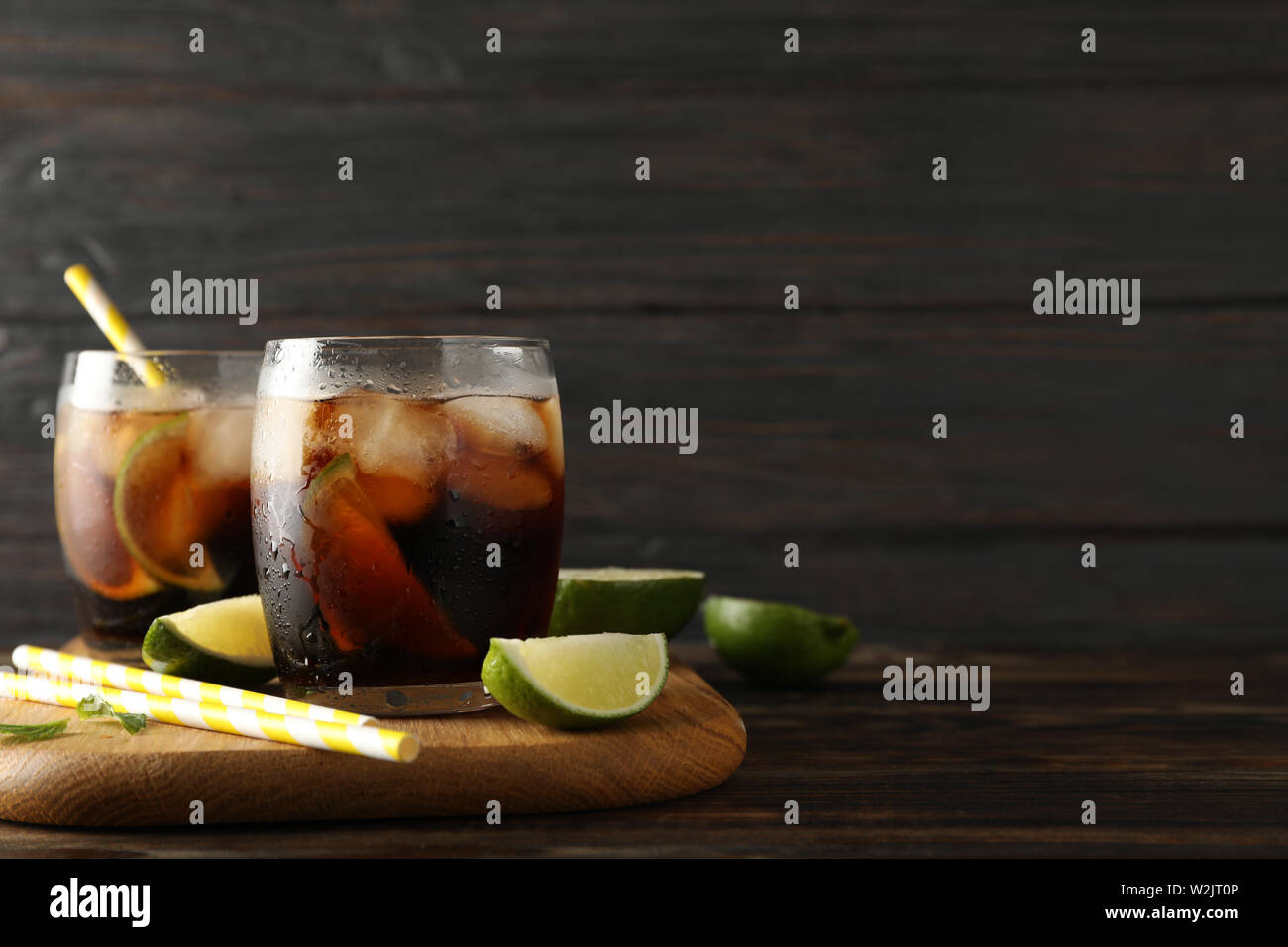 Bicchieri con ghiaccio cola, fettine di lime e di tubuli su sfondo di legno Foto Stock