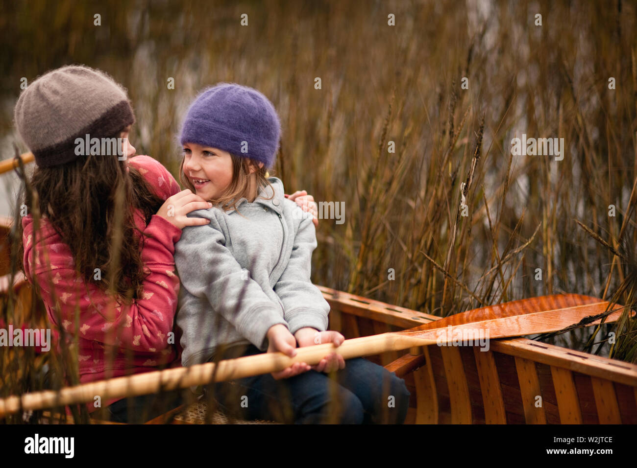 Giovani suore il sorriso a vicenda come si siedono insieme in una canoa di legno tra ance su un lungolago e posare per un ritratto. Foto Stock