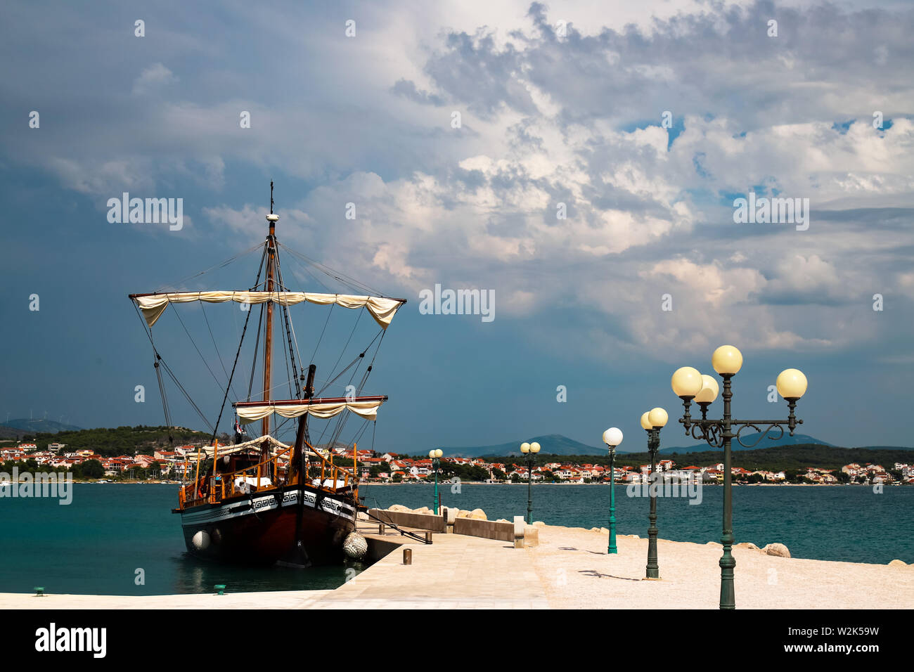 Bellissimo legno marrone yacht vicino al molo con lanterne in mare azzurro e limpido, pittoresco nuvole di Sibenik, Croazia. Viaggi croato, mare e estate Foto Stock