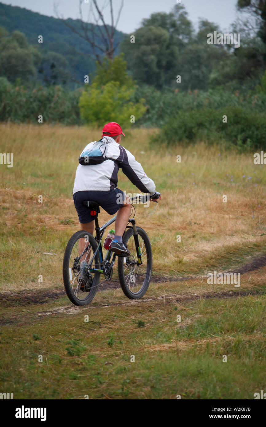 Kharkiv, Ucraina - Luglio 06, 2019: vista posteriore di un uomo in sella a una moto su una strada sterrata in un campo nei pressi della foresta Foto Stock