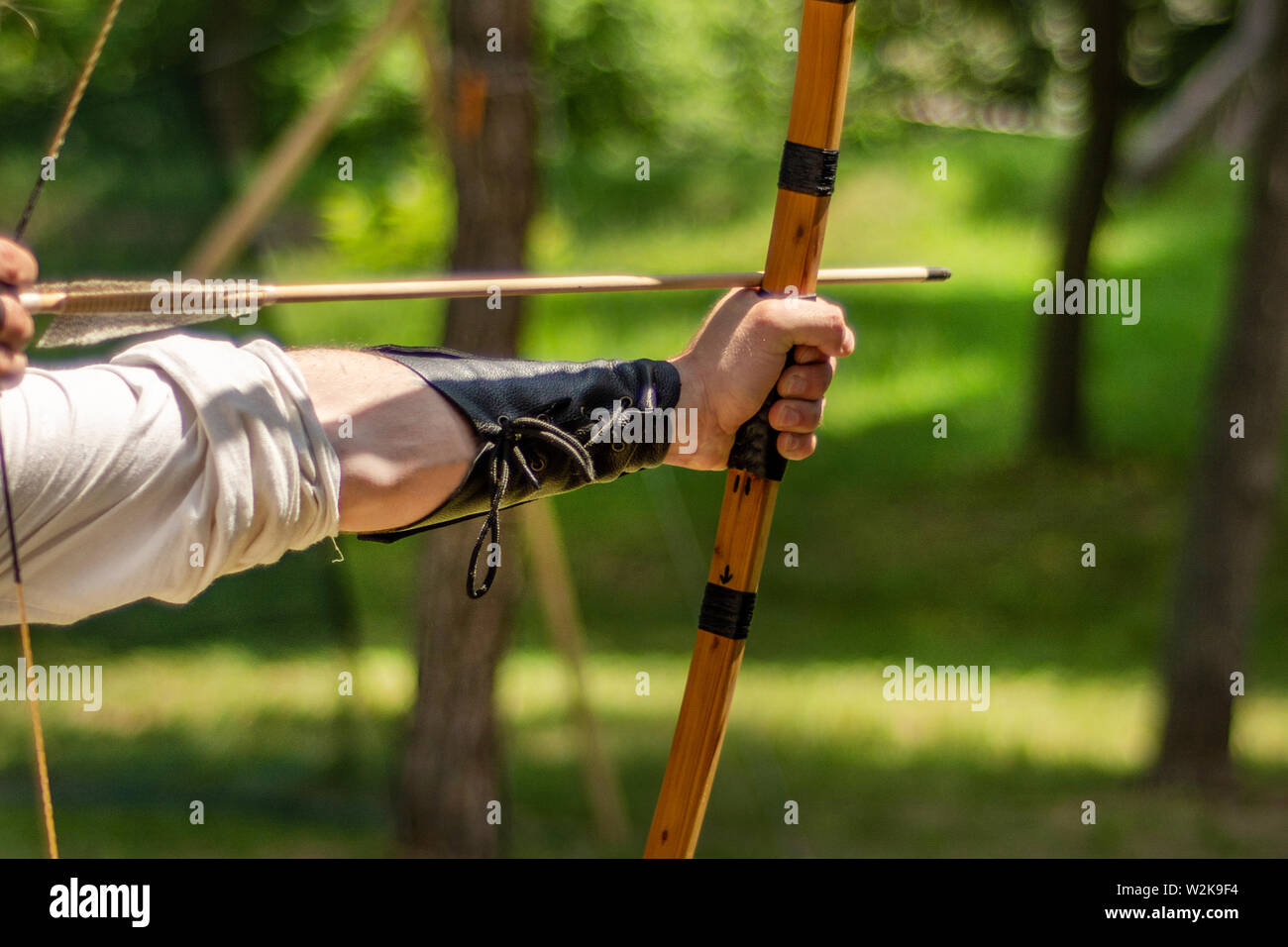 Archer mano trattiene il suo arco con una freccia e mirando all'obiettivo l'attività all'aperto nella foresta. Medieval sport concept. Close up, il fuoco selettivo Foto Stock