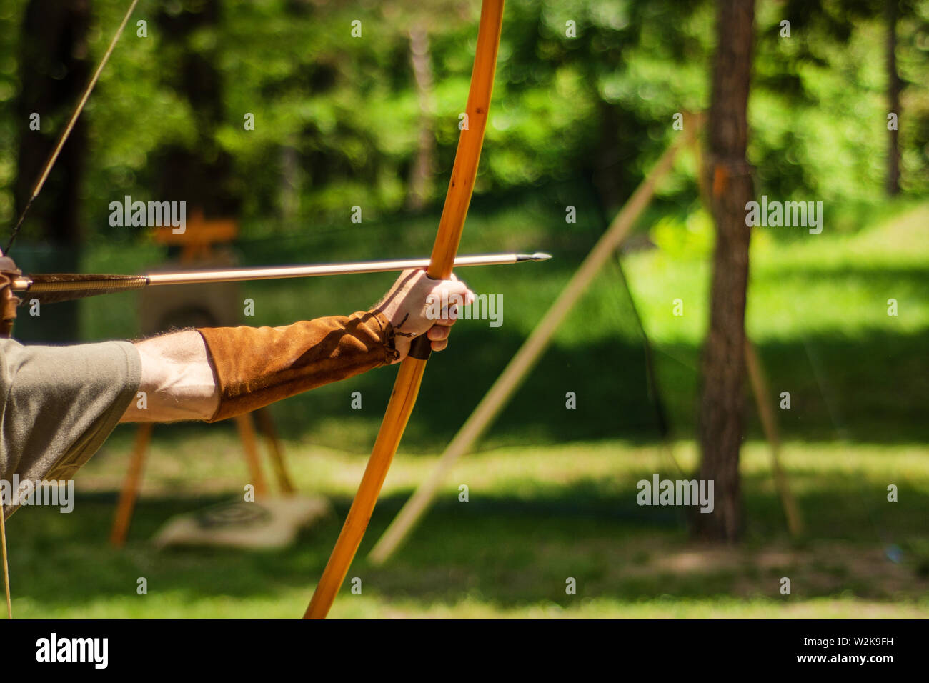 Uomo arciere medievale mano trattiene il suo arco con una freccia e mirando all'obiettivo l'attività all'aperto nella foresta. Medieval sport concept. Close up Foto Stock