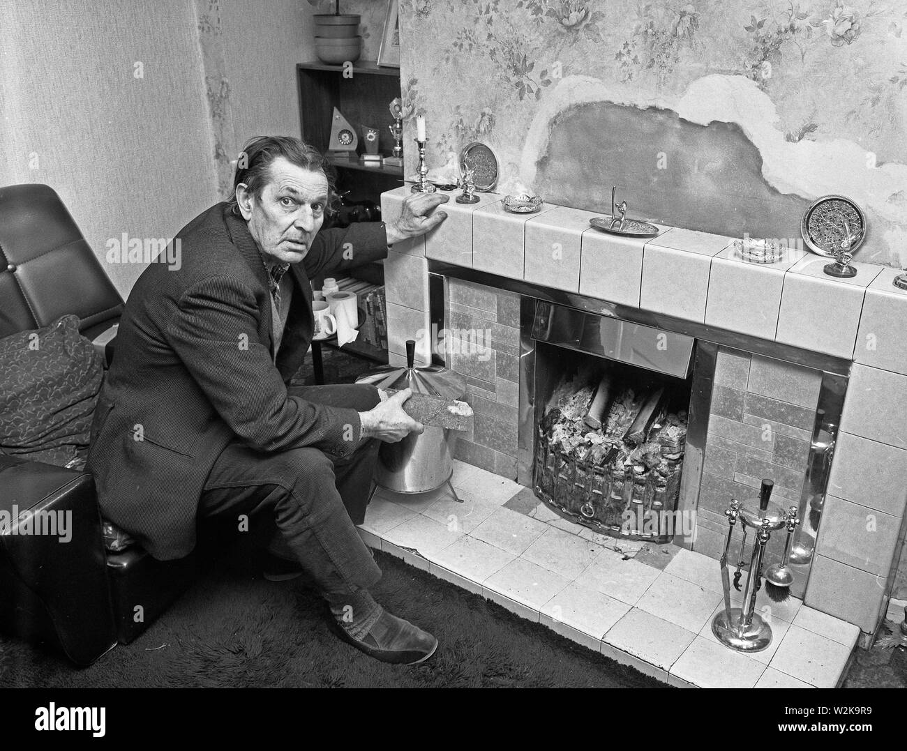 Uomo anziano che cerca di tenersi al caldo con un fuoco aperto nel North Yorkshire, Gran Bretagna 1985. bollette del carburante costi di riscaldamento rimborso carburante invernale Foto Stock