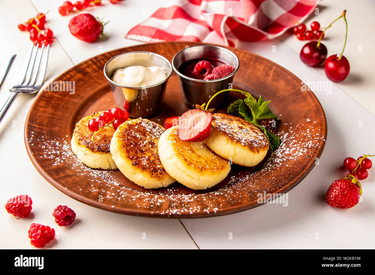 Cottage cheese pancakes, fatti in casa tradizionale piatto ucraino syrniki con salsa di frutti di bosco e panna acida su una piastra marrone su sfondo bianco Foto Stock