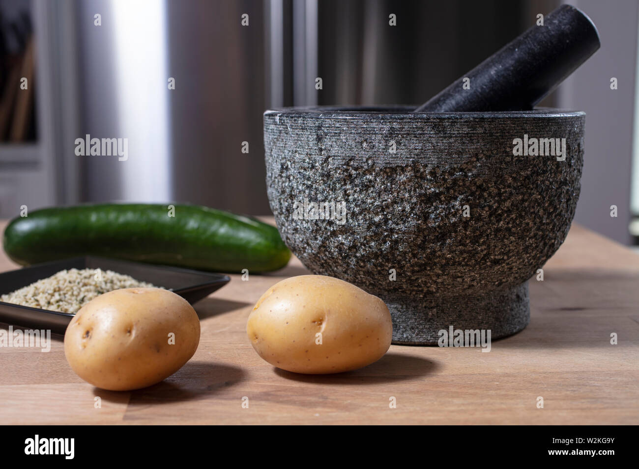 Mortaio e pestello di pietra su un bancone cucina con potatoe, sementi di canapa e di cetriolo Foto Stock