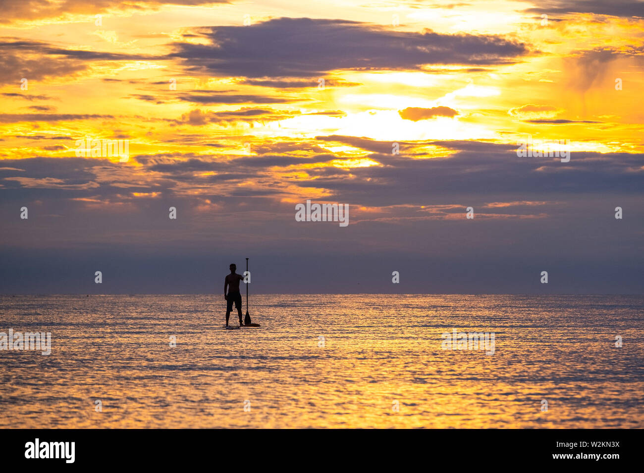 Aberystwyth Wales UK, martedì 09 luglio 2019 UK Meteo: un uomo stagliano contro i colori del tramonto come essi paddleboard sulla calma piatta mare sulla spiaggia in Aberystwyth alla fine di una calda giornata d'estate nel Galles occidentale. Photo credit: Keith Morris//Alamy Live News Foto Stock