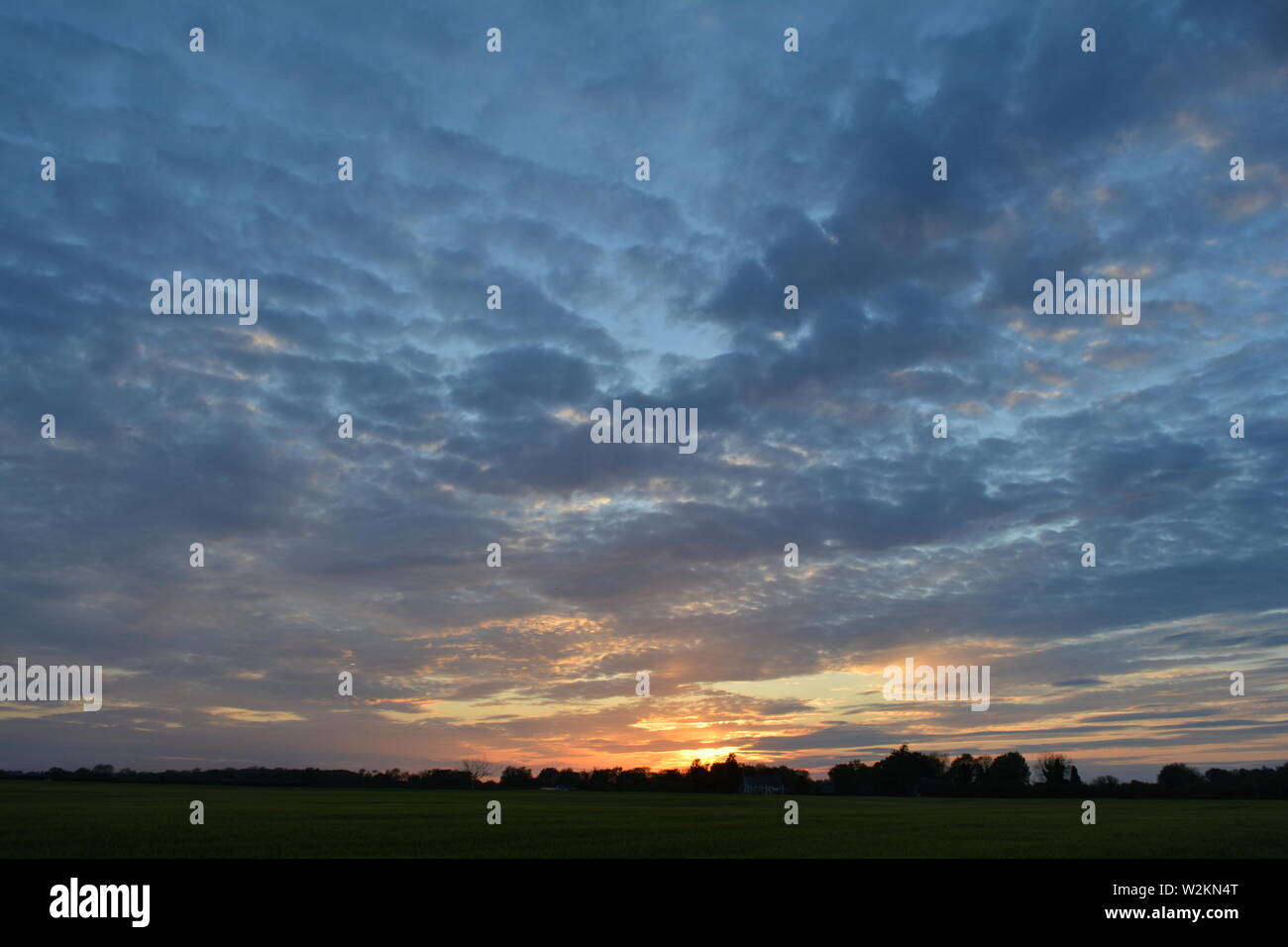 Una collezione di foto del sole che tramonta sui campi piani di Suffolk con un bel motivo a nuvole che si estende attraverso il cielo. Foto Stock