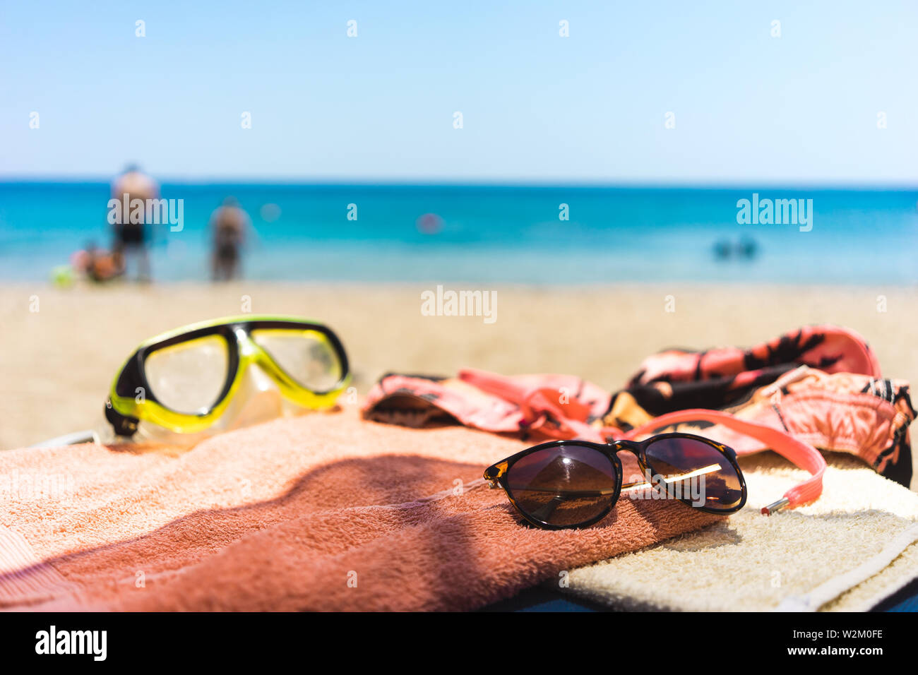 Vacanze estive: asciugamano con spiaggia di diversi accessori come occhiali da sole, occhialini e costume da bagno all'oceano Foto Stock