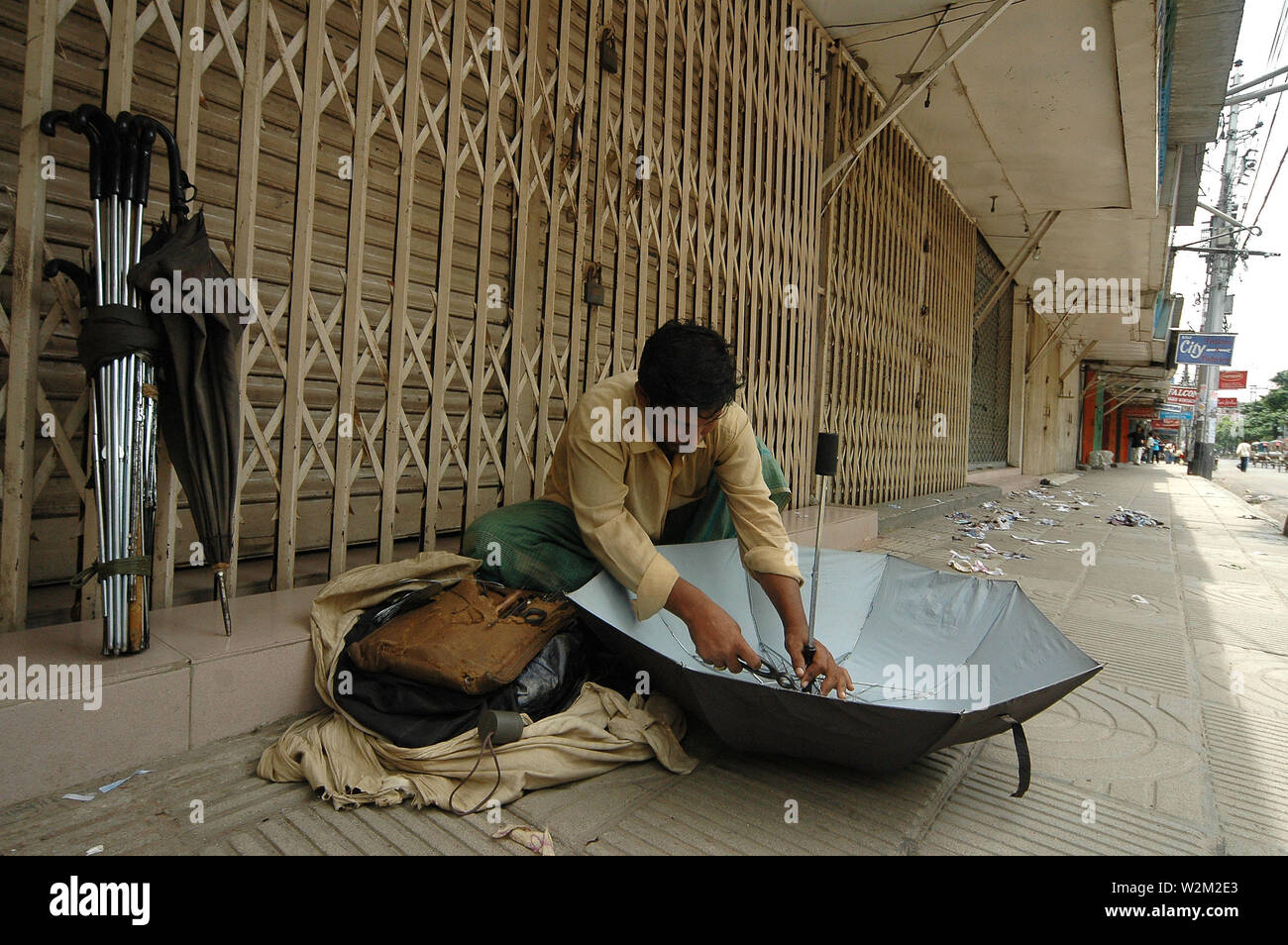 Un ombrello mender rammendo un ombrello a nuova strada di elefante, Dhaka, Bangladesh. Luglio 16, 2005. Foto Stock