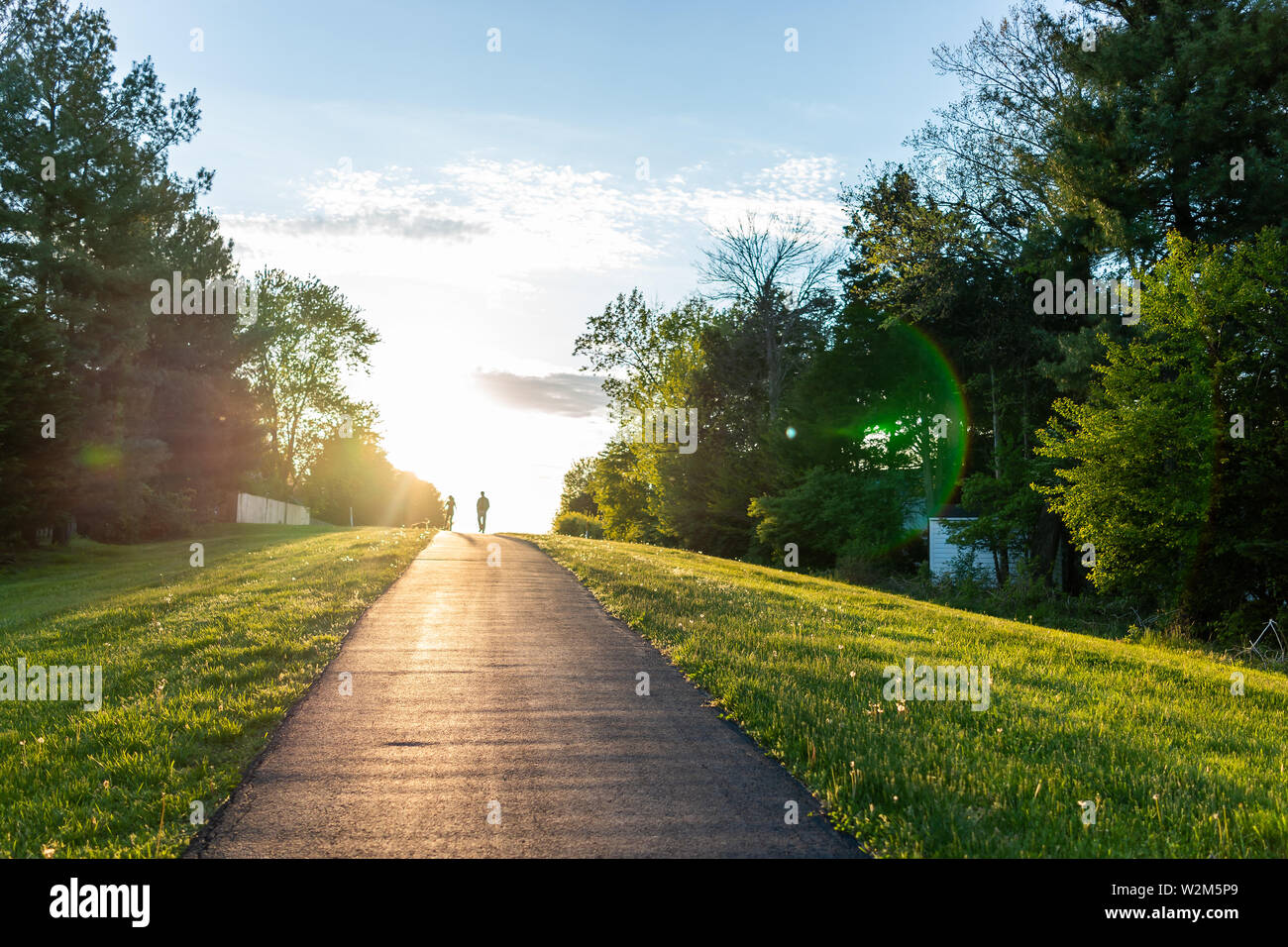 Sugarland eseguire Stream Valley Trail escursione in Herndon, Virginia, Fairfax County in primavera con il sentiero lastricato stradale e silhouette di un giovane a piedi Foto Stock