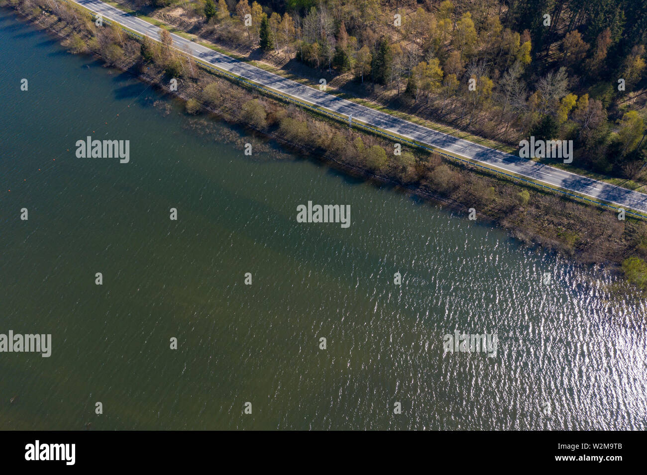 Vista aerea di un paese asfaltata strada lungo il bordo di un territorio densamente boscosa sulla montagna della banca di una diga, drone shot Foto Stock