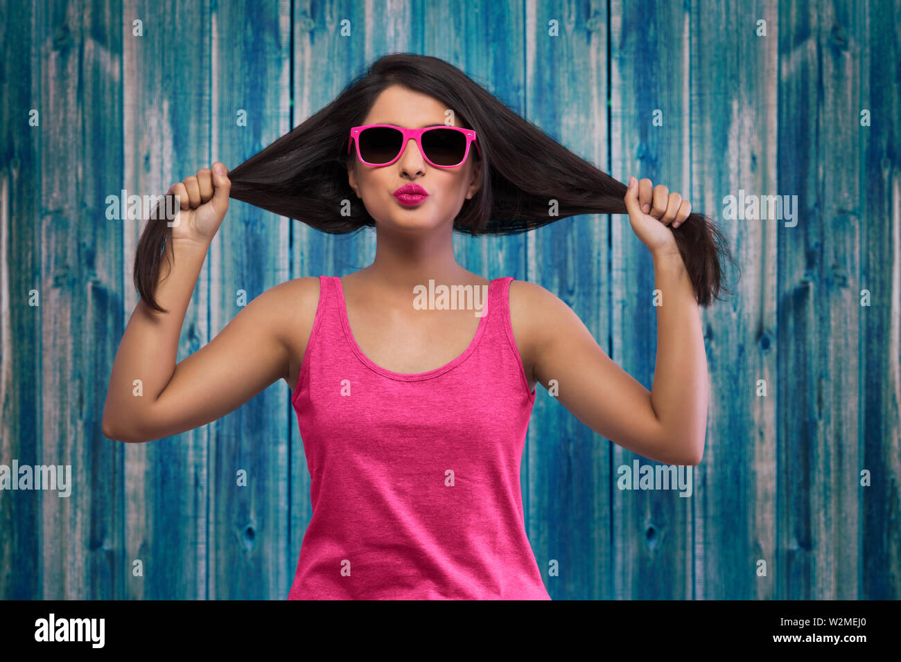 Ritratto di giovane ragazza in rosa top e fantasiosi occhiali tenendo i capelli ai suoi lati Foto Stock