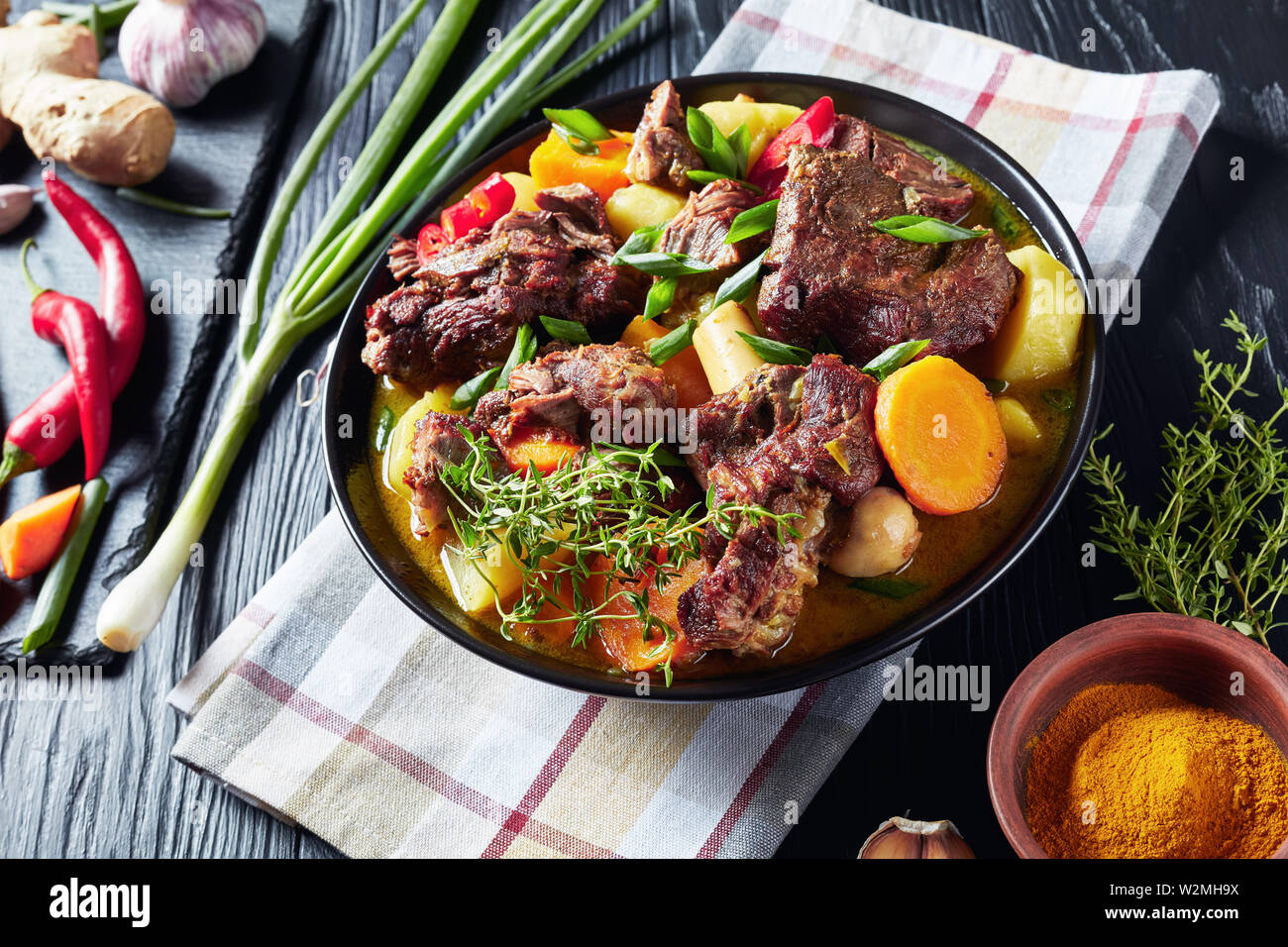 Tradizionale giamaicana di capra al Curry - slow cotto speziato giamaicano di carni e verdure al curry piccante in una ciotola nero su una tavola in legno rustico, close-up Foto Stock