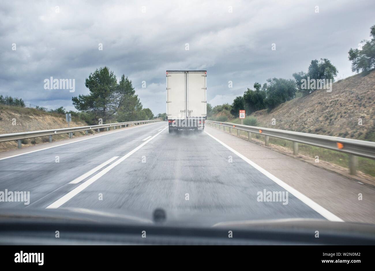 Guida dietro lento carrello su strada locale in un giorno di pioggia. Vista dall'interno della vettura. Foto Stock