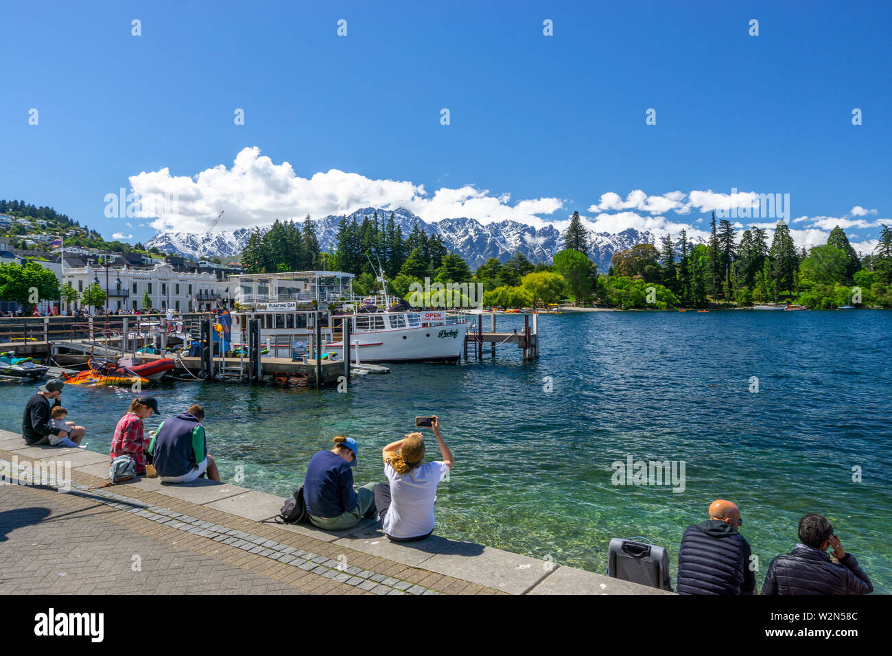 I turisti seduti sul litorale del lago di Wakatipu in Queenstown sulla giornata di sole, Isola del Sud della Nuova Zelanda Foto Stock