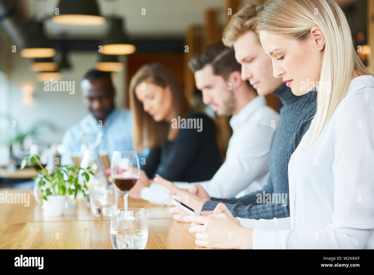 Giovani con telefono cellulare dipendenza nel ristorante sono costantemente alla ricerca di loro smartphone Foto Stock
