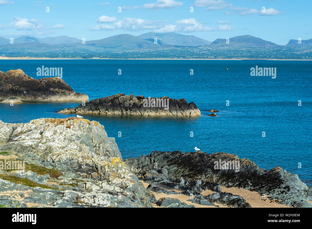 Lo stretto di Menai e le montagne Snowdonia sullo sfondo viste dalla costa rocciosa di Anglesey Island in estate nel Regno Unito Foto Stock