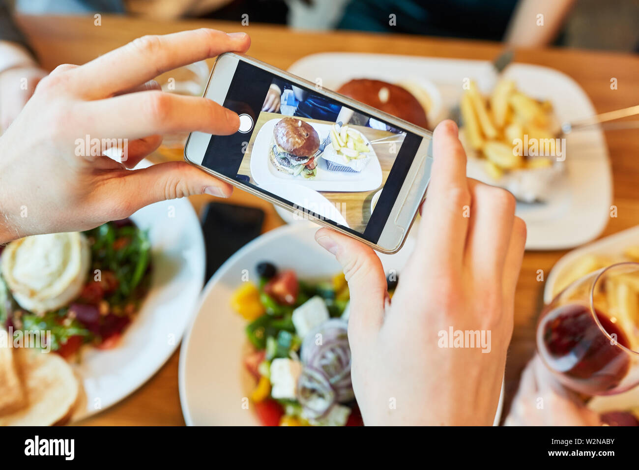 Fotografare mani per mangiare nel ristorante utilizzando un telefono cellulare o smartphone Foto Stock