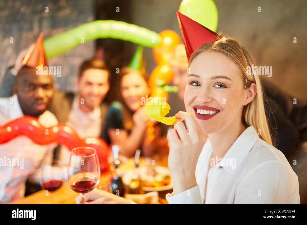 Donna sorridente con una tromba a carnevale o festa di carnevale con gli amici Foto Stock