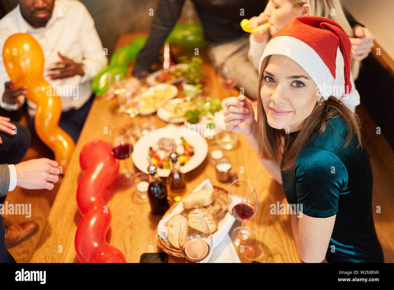 Giovane donna con cappello da Babbo Natale con i tuoi amici a cena ad una festa di natale Foto Stock