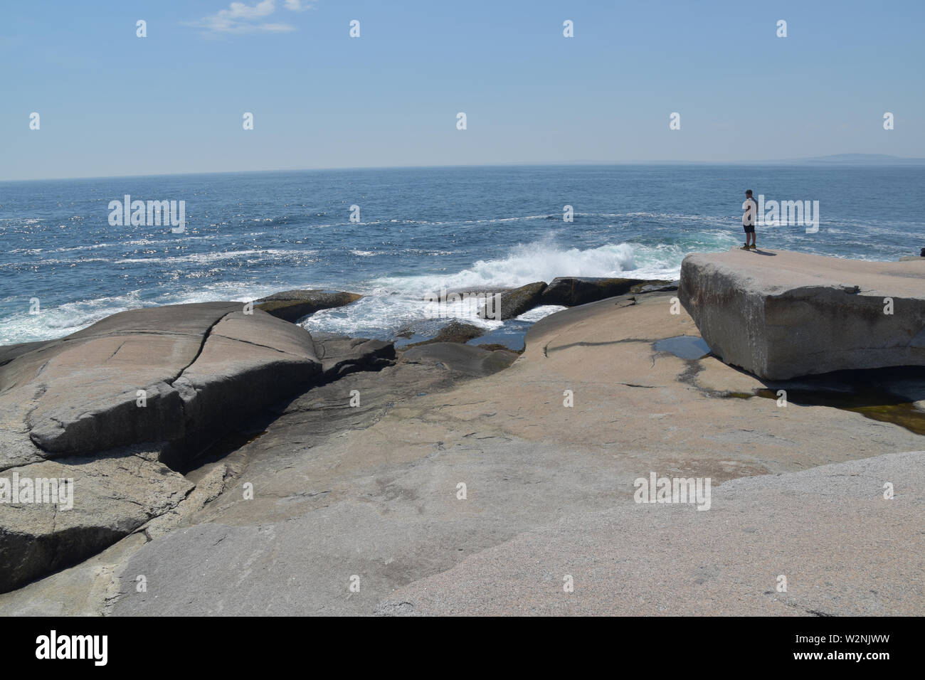 Uomo in piedi su masso di granito che guarda il mare Foto Stock