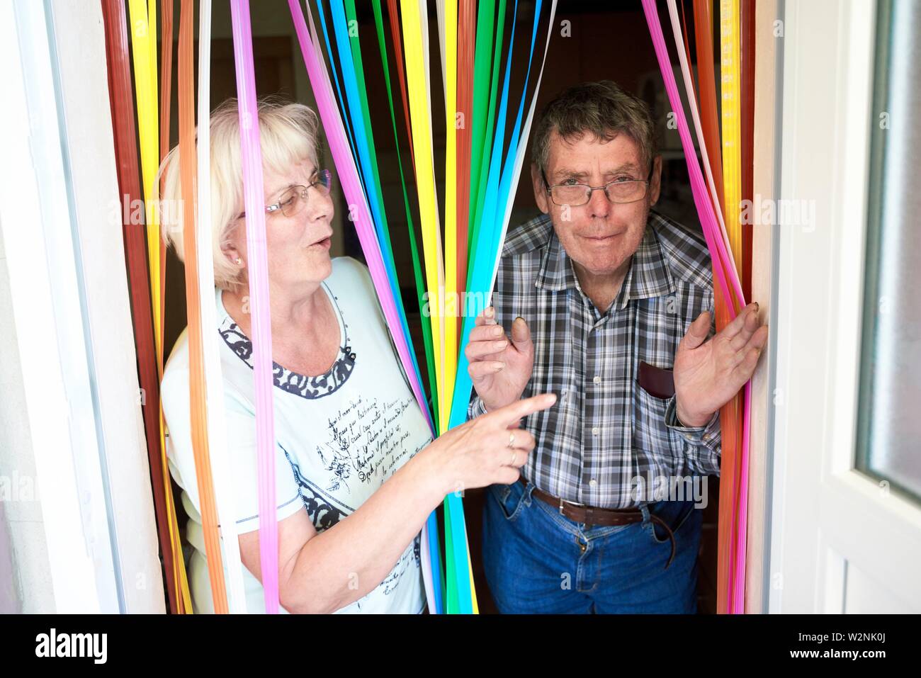 Divertente coppia senior a piedi attraverso colorate strisce tenda a casa Foto Stock